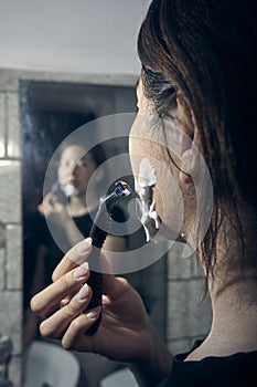 Woman with razor and shaving foam on her face