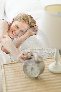 Woman Reaching For Alarm Clock While Lying On Bed