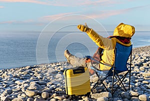 Woman reaching the destination and sitting on beach chairs on the seaside at sunrise. British cold