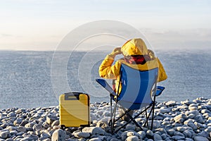 Woman reaching the destination and sitting on beach chairs on the seaside at sunrise. British cold