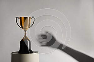 Woman reaching for gold trophy cup on light background, closeup