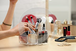 Woman reaching for organizer with cosmetic products and makeup accessories on dressing table indoors
