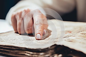 Woman reading ancient book - Bible. Concentrated attentively follows finger on paper page in library. Old archival