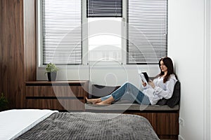 Woman reading book in a bedroom with bed and wooden wardrobe in modern apartment