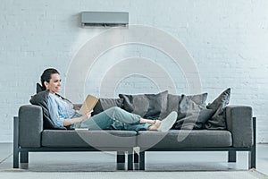 woman reading book on couch air conditioner blowing