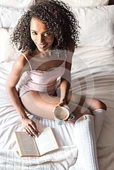Woman reading a book and drinking coffee on bed with socks