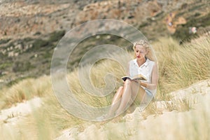 Woman reading book, enjoying sun on beach.