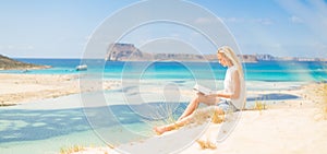 Woman reading book, enjoying sun on beach.