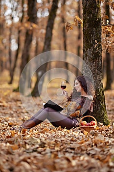 Woman is reading a book with a glass of wine in her hand during autumn