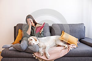 Woman reading a book while her pet dog is lying next to her