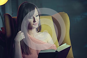 Woman reading book at home in dark cosy room