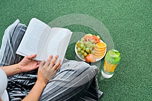 Woman reading book on the lawn, top view over shoulder