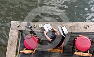 Woman reading a book lying and drink ice coffee on the chair in wood terrace against beautiful view relax and happy day,