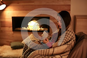 Woman reading book near decorative fireplace at home.