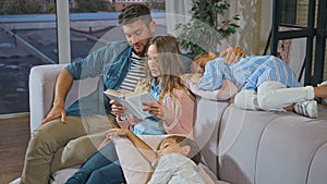Woman reading book near husband and children sleeping in living room.