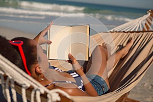 Woman reading a book while relaxing on hammock on beach