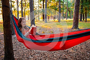 Woman reading a book, relaxing on the hammock in forest, leisure time and summer holiday concept