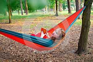 Woman reading a book, relaxing on the hammock in forest, leisure time and summer holiday concept