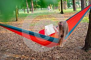 Woman reading a book, relaxing on the hammock in forest, leisure time and summer holiday concept