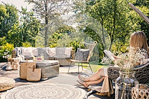 Woman reading book while relaxing at terrace with rattan furniture in the garden. Real photo photo