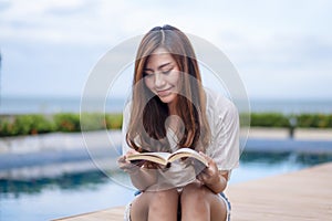 A woman reading book by swimming pool with feeling relaxed