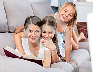 Woman reading book to daughters on sofa