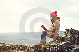 Woman reading book on the top of rock in autumn day.