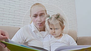 Woman reading a children`s book for a little girl sitting with a child on the couch