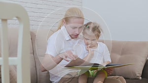 Woman reading a children`s book for a little girl sitting with a child on the couch