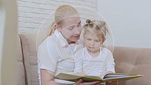 Woman reading a children`s book for a little girl sitting with a child on the couch