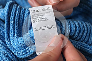 Woman reading clothing label with care symbols on knitted sweater, closeup