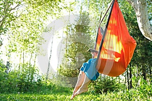 Woman reading e-book or using tablet while sitting in hammock chair on nature on sunset. Cottagecore, slow life in countryside,