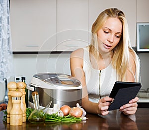 Woman reading ereader and cooking with crockpot