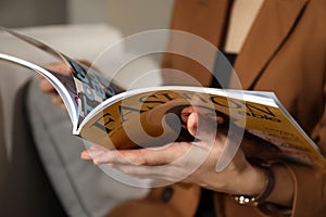 Woman reading fashion magazine on sofa at home, closeup