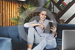 Woman reading funny content on tablet. Young lady relaxing at home, commenting in social networks, watching entertaining videos.