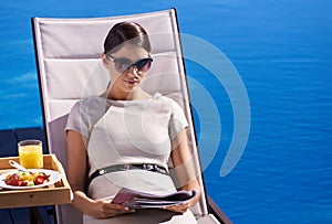 Woman, reading and magazine on sunbed outdoor with sunglasses for relax, snacks and lifestyle news. Person, publication