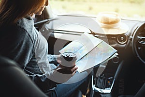 A woman reading a map for direction and drinking coffee in the car