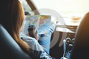 A woman reading a map for direction and drinking coffee in the car