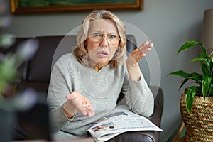 Woman reading newspaper at home, shocked and surprised over the news. Mature woman