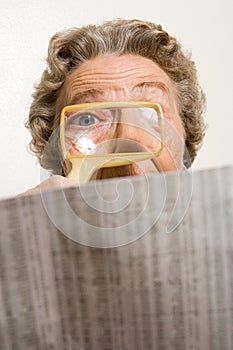 Woman reading newspaper with magnifying glass