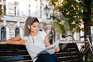 Woman reading newspaper while sitting on the bench