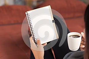 Woman reading notebook and holding coffee cup