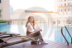 Woman reading and relaxing near luxury swimming pool