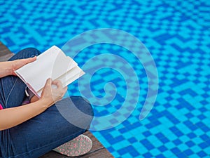 Woman reading and relaxing near luxury swimming pool