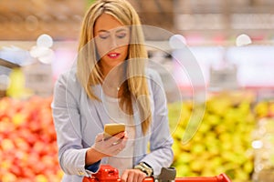 Woman reading shopping list on her phone while shopping in supermarket