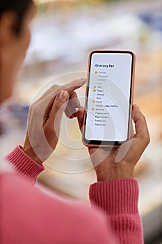 Woman reading shopping list on smartphone screen in supermarket