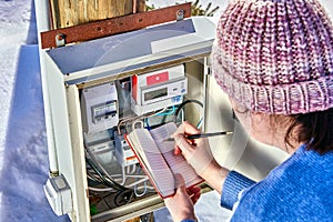 Woman readings from external electric meter outdoors.