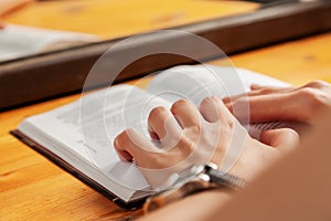 A woman reads a book before going to bed. Women`s hands are holding a book in close-up. An open paper book is lying on the table