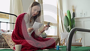 Woman reads the instructions of the pill, sitting on the bed covered with a blanket