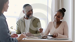 Woman real estate agent preparing rental contract for happy african american couple, smiling woman signing agreement